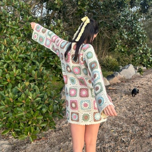 Girl wearing flower granny square crochet dress with back facing camera and arms outstretched.