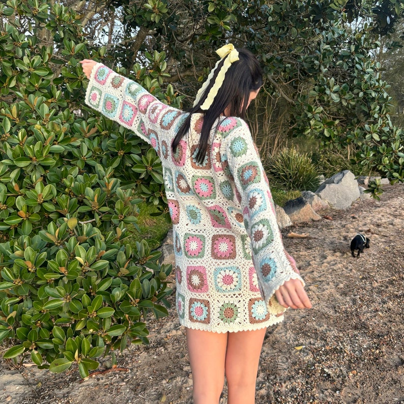 Girl wearing flower granny square crochet dress with back facing camera and arms outstretched.