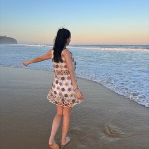 Girl in crochet flower dress standing at beach from the back with arms outstretched.