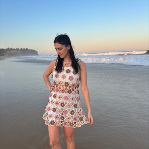 Girl in crochet flower dress standing at beach looking to left.
