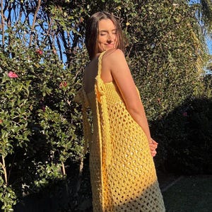 Peut inclure: Une robe jaune au crochet avec un d&eacute;collet&eacute; halter et un motif ajour&eacute;. La robe a une coupe d&eacute;contract&eacute;e et est port&eacute;e &agrave; l'ext&eacute;rieur &agrave; la lumi&egrave;re naturelle. La robe est de couleur jaune vif unie.