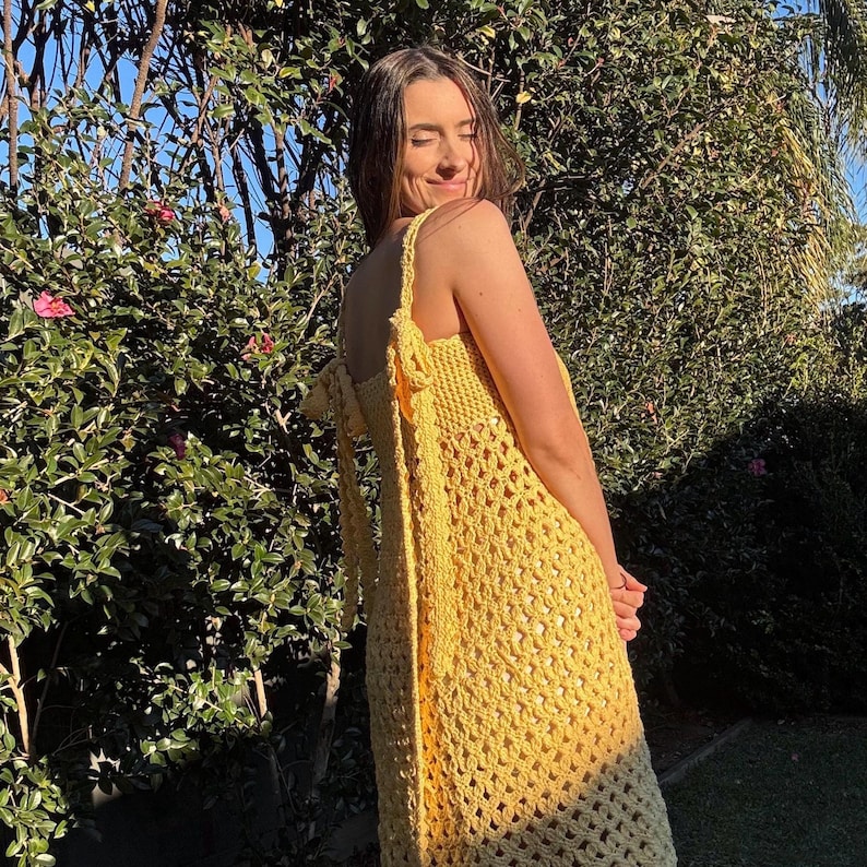 Peut inclure: Une robe jaune au crochet avec un d&eacute;collet&eacute; halter et un motif ajour&eacute;. La robe a une coupe d&eacute;contract&eacute;e et est port&eacute;e &agrave; l'ext&eacute;rieur &agrave; la lumi&egrave;re naturelle. La robe est de couleur jaune vif unie.
