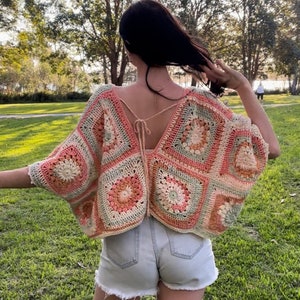 Pode incluir: Um top de croch&ecirc; com um padr&atilde;o quadrado em tons de rosa, verde e branco. O top tem um la&ccedil;o na parte de tr&aacute;s do pesco&ccedil;o e &eacute; usado sobre um short jeans.