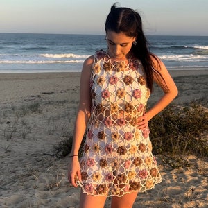 Girl in crochet flower dress standing at beach looking down.