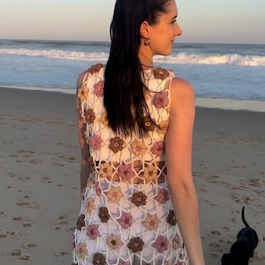 Girl in crochet flower dress from back standing at beach looking to right.