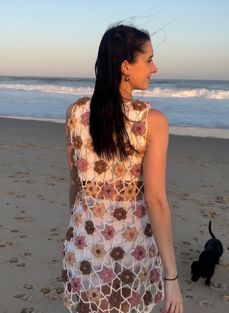Girl in crochet flower dress from back standing at beach looking to right.