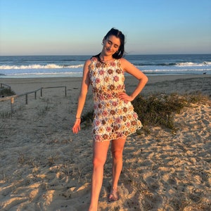 Girl in crochet flower dress standing at beach with hand on hip.