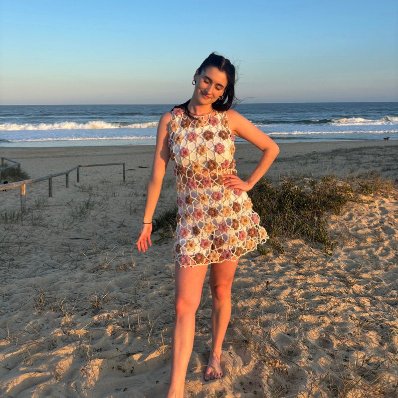 Girl in crochet flower dress standing at beach with hand on hip.