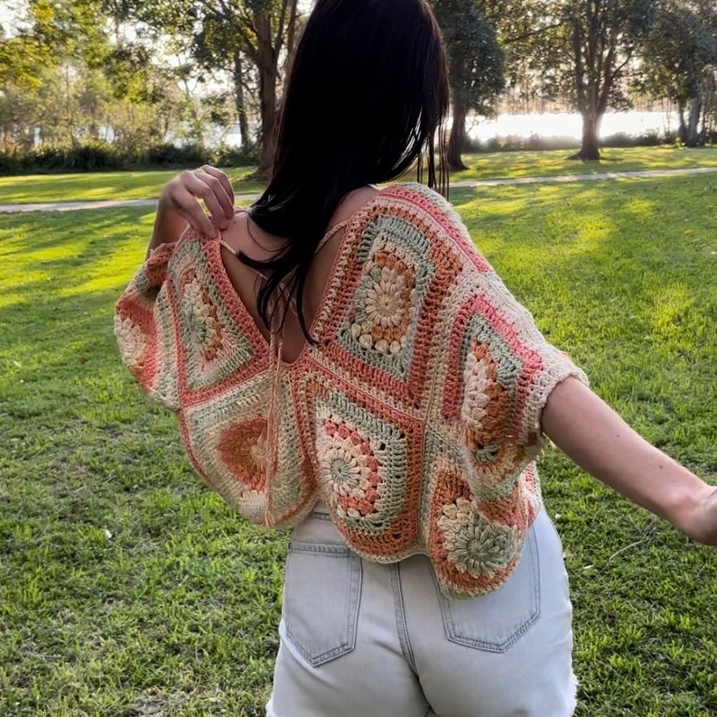 Pode incluir: Um top de croch&ecirc; com um padr&atilde;o de quadrado da vov&oacute; em tons de p&ecirc;ssego, creme e verde. O top tem um decote em V e mangas curtas.