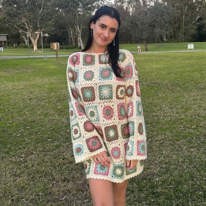 Girl wearing flower granny square crochet dress smiling at the camera in a park.