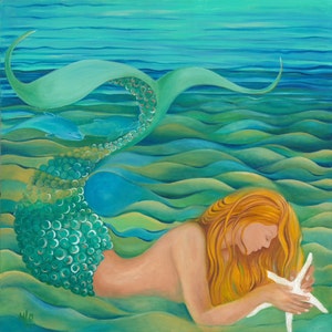 Redhead mermaid with aqua tail lying down admiring starfish in the blue green water