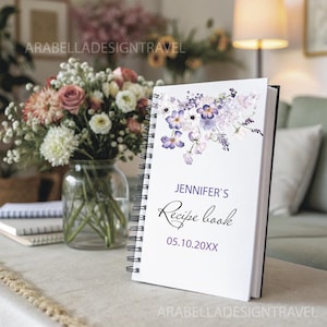 May include: A white spiral bound recipe book with a watercolor floral design in shades of purple and white. The text on the cover reads "Jennifer's Recipe Book 05.10.20XX".