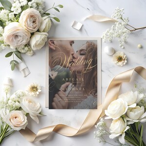 Puede incluir: Una invitaci&oacute;n de boda con una foto de una pareja bes&aacute;ndose. La invitaci&oacute;n est&aacute; decorada con caligraf&iacute;a dorada y el texto "The Wedding of Abigail Belle Morgan & Michael Dale Johnson".