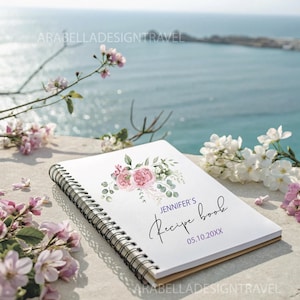 May include: A white spiral bound recipe book with a watercolor floral design featuring pink roses and green leaves. The text "Jennifer's Recipe Book" is written in black cursive with the date "05.10.20XX" below it.