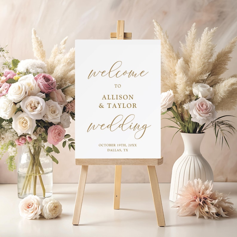 Puede incluir: Se&ntilde;al de bienvenida de boda blanca con texto en caligraf&iacute;a dorada. El letrero dice "Bienvenido a Allison & Taylor Wedding, 19 de octubre de 20XX, Dallas, TX".