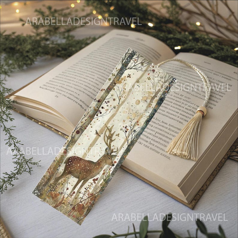 May include: A rectangular bookmark featuring a watercolor illustration of a deer in a forest scene. The bookmark has a cream-colored tassel attached. The text "ARABELLADESIGNTRAVEL" is printed on the bookmark.
