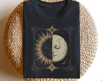Op de afbeelding: Zwart T-shirt met een gouden en witte illustratie van een zon en maan met een gezicht. De illustratie is omlijst met een decoratieve rand.