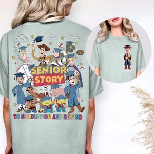May include: Pale green t-shirt with a vibrant graphic of Toy Story characters celebrating graduation. The design includes the text "SENIOR STORY" and "TO GRADUATION AND BEYOND". A small image of Woody in a graduation gown is on the front.
