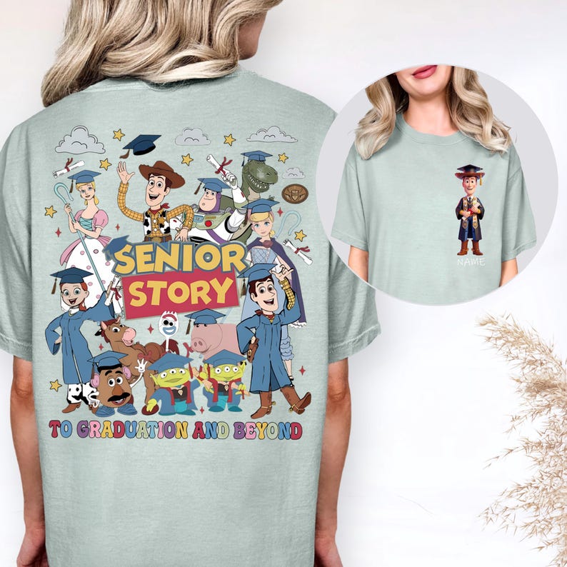 May include: Pale green t-shirt with a vibrant graphic of Toy Story characters celebrating graduation. The design includes the text "SENIOR STORY" and "TO GRADUATION AND BEYOND". A small image of Woody in a graduation gown is on the front.
