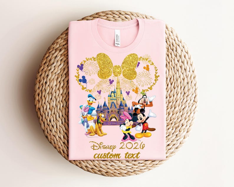 K&ouml;nnte beinhalten: Hellrosa T-Shirt mit goldener Glitzer-Schleife und Feuerwerk-Design, Disney-Figuren und einem Schloss. Der Text "Disney 2020 custom text" ist in Gold gedruckt.
