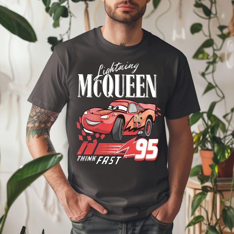 May include: Dark gray t-shirt featuring Lightning McQueen from the Cars movie. The design includes the text "Lightning McQueen", a red race car, the number "95", and the words "Think Fast".