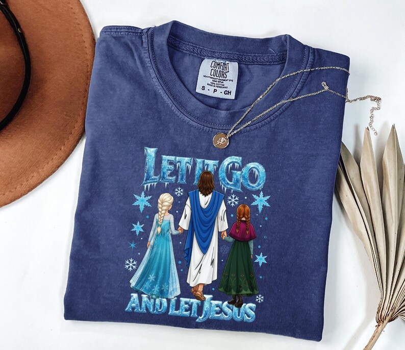 May include: A navy blue t-shirt with the text "LET IT GO AND LET JESUS" in blue and white. The graphic depicts Jesus with two girls in blue and green dresses. A gold necklace and a brown hat are also visible.
