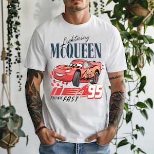 May include: White t-shirt featuring a graphic of Lightning McQueen from the Cars movie. The design includes the text "Lightning McQueen" above a red race car with the number "95" and the words "Think Fast".
