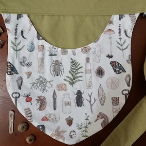May include: A white fabric pouch with a green fabric strap. The pouch is decorated with a variety of nature-themed illustrations, including insects, plants, and seashells.