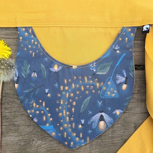 May include: A blue fabric bib with a yellow trim and a pattern of fireflies, leaves, and a net. The bib is tied with a long yellow fabric strap.
