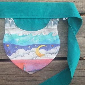 May include: Teal fabric sash with a crescent moon and clouds design. The fabric is printed with a watercolor-like effect and features a desert landscape with a cactus.