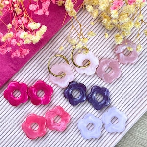 Pode incluir: Um conjunto de seis pares de brincos em forma de flor em várias cores, incluindo rosa, roxo e branco. Os brincos são feitos de resina e têm um aro dourado.