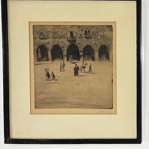 May include: An antique framed print depicting a detailed architectural scene with arched doorways and figures. The artwork, in shades of sepia and black, is set against a cream-colored mat and enclosed in a black frame, creating a classic aesthetic.