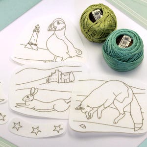 Puede incluir: Parches de bordado con dibujos lineales de un frailecillo, un faro, un castillo, una liebre, un zorro, una luna y estrellas. También hay dos carretes de hilo de bordar verde y verde azulado.