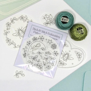 May include: An embroidery kit featuring pre-printed designs of bees, flowers, and botanical elements. The kit includes green thread and a package labelled "Slick & Stitch Embroidery Patterns". The designs are printed on white fabric.
