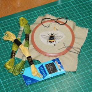 Layout with embroidery scissors, threads, needles and a worked patch with a bee design.