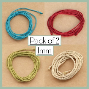 Könnte beinhalten: Ein Pack mit zwei 1 mm dicken Schnüren in vier Farben: Türkis, Rot, Grün und Beige. Die Schnüre sind zu Kreisen gewickelt und auf einem braunen Hintergrund abgebildet.