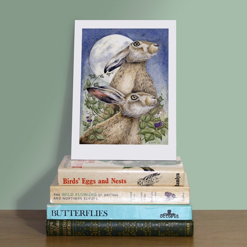 A5 art print of two British badgers propped up on a pile of nature books against a pale green wall.