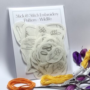 18 Wildlife Stick & Stitch embroidery patterns on self adhesive water soluble stabilizer - badger, fox, hare, butterfly, leaves beside threads and scissors.