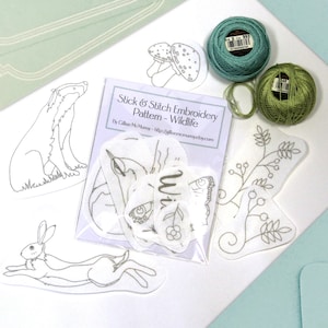 18 Wildlife Stick & Stitch embroidery patterns on self adhesive water soluble stabilizer beside some threads.