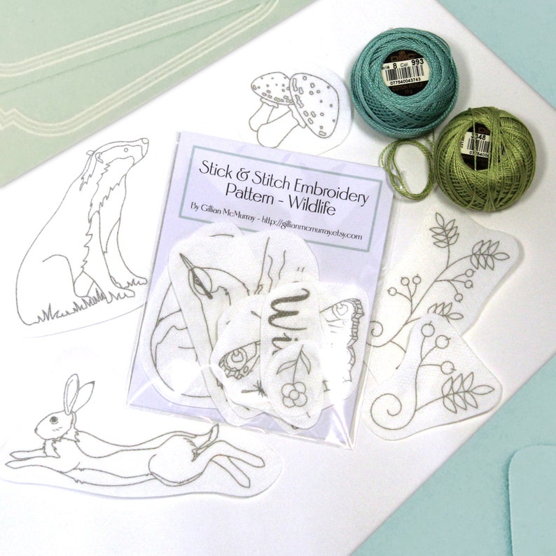 18 Wildlife Stick & Stitch embroidery patterns on self adhesive water soluble stabilizer beside some threads.
