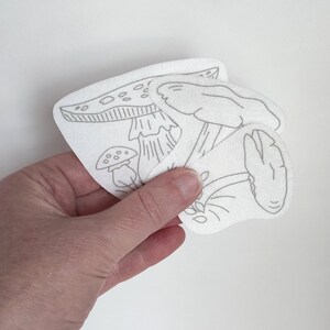 Three large fungi Stick & Stitch embroidery patterns on self adhesive water soluble stabilizer held in a hand to show size.