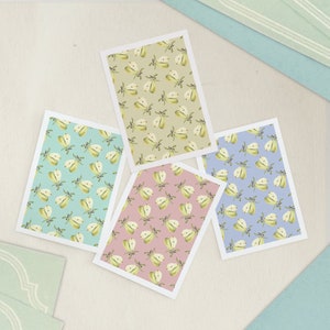 May include: Four rectangular cards featuring a repeating pattern of halved pears with green leaves. The cards have backgrounds in light green, teal, dusty pink, and periwinkle blue, each framed by a thin white border on a textured surface.