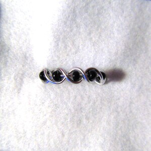 Puede incluir: Un anillo de alambre plateado con cuentas negras tejidas en el diseño.