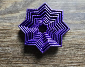 May include: A layered, purple star-shaped object with a nested design. The object has a series of star shapes decreasing in size towards the center. The object is made of a solid material and sits on a wooden surface.