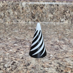 May include: A black and white cone-shaped object with a spiral design. The object is primarily black with white stripes that wrap around the cone. The base is solid black, and the top is white. The object is likely a decorative item.