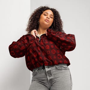 May include: A red cropped jacket with a zipper closure and a drawstring waist. The jacket is covered in a repeating pattern of red symbols.