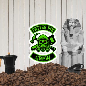 Puede incluir: Una pegatina con el texto "Pattes Fix Crew" y un diseño de máscara de gas verde con un martillo y una llave. La imagen también incluye una cafetera negra, una estatua blanca de un faraón y dos tazas de café negras, todo sobre un lecho de granos de café.