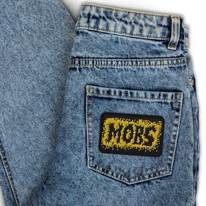 May include: Blue denim jeans with a yellow embroidered patch on the back pocket that says "MÖRB".