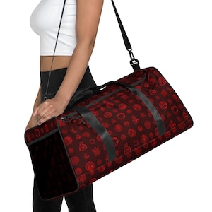 Puede incluir: Una bolsa de lona granate con un patrón rojo repetido de formas circulares y abstractas. La bolsa tiene correas negras y una correa para el hombro. La bolsa se lleva sobre el hombro.