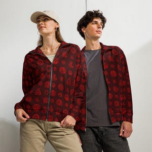 May include: Two people wearing matching burgundy zip-up jackets with a repeating red pattern. The jackets have a high collar and a full-length zipper. The pattern consists of various circular and abstract shapes.